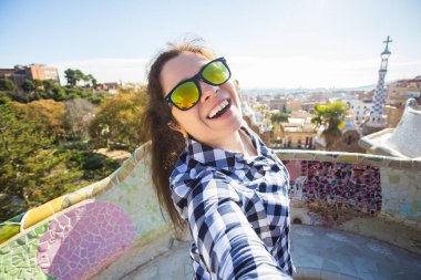 Seyahat ve tatil kavramı - kamera çekimi fotoğraf Park Guell, Barselona, İspanya, gülümseyen akıllı telefon ile arayan güzel genç kadın.