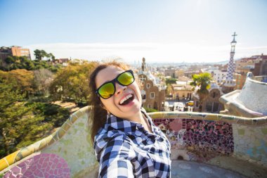 Seyahat ve tatil kavramı - kamera çekimi fotoğraf Park Guell, Barselona, İspanya, gülümseyen akıllı telefon ile arayan güzel genç kadın.