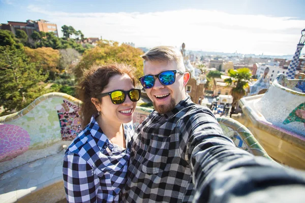 Pareja joven y divertida mirando a la cámara tomando fotos con el teléfono inteligente sonriendo en Park Guell, Barcelona, España . — Foto de Stock