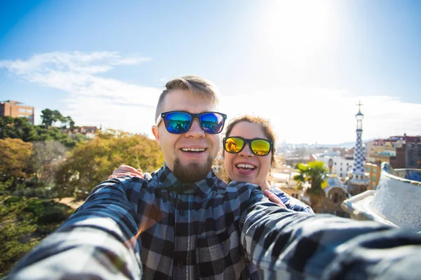 Komik genç çift kamera ile akıllı telefon Park Guell, Barselona, İspanya, gülümseyen fotoğrafı çekmek.