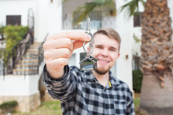 Dwelling, buying home, real estate and ownership concept - handsome man showing his key to new home — Stock Photo, Image