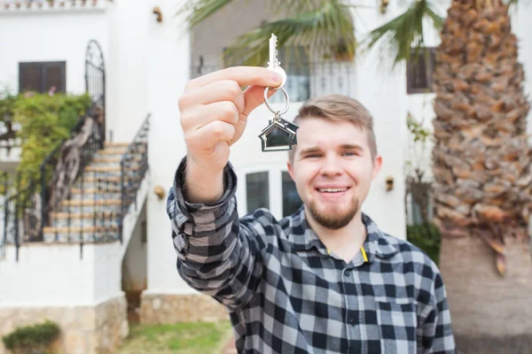 Property, ownership, new home and people concept - young man with keys standing outside new home