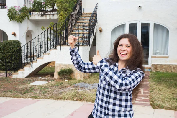 Vastgoed en eigenschap concept. Gelukkig eigendom. Aantrekkelijke jonge vrouw houden van sleutels terwijl permanent buiten tegen nieuwe huis. — Stockfoto