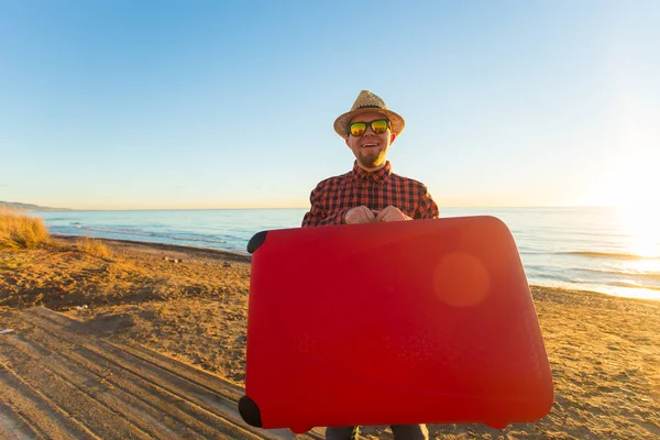 Concepto de viaje y verano - Turista masculino llevando una maleta roja en la playa — Foto de Stock