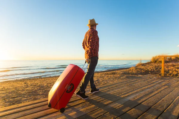 Gente, viaje y concepto de vacaciones - retrato del hombre feliz caminando por el mar con la maleta — Foto de Stock