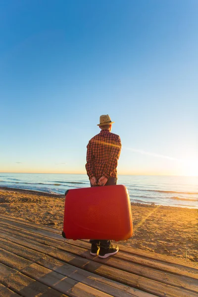 Viajes, vacaciones y concepto de verano - Vista trasera del hombre sosteniendo una maleta al atardecer — Foto de Stock