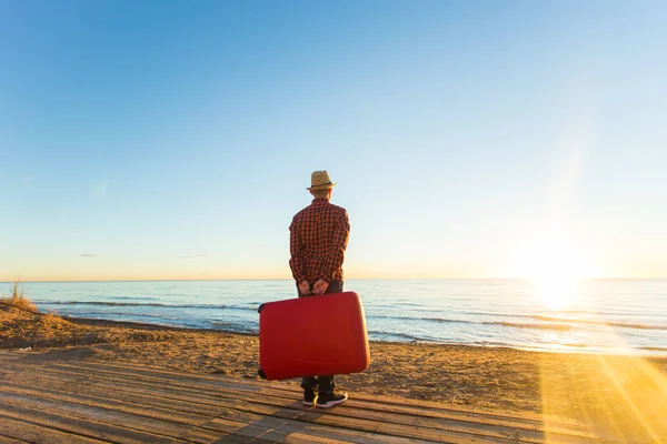 Concepto de vacaciones, viajes y turismo - Hombre guapo con maleta roja sobre fondo de playa de arena — Foto de Stock