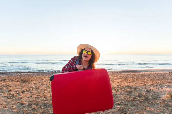 Viajes, vacaciones y concepto de vacaciones - Mujer joven divertida sosteniendo la maleta en la playa — Foto de Stock