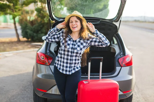 Reisen, Urlaub und Menschen-Konzept - junge Frau steht lächelnd in der Nähe des Autos und macht sich bereit, ihren Hut zu halten — Stockfoto