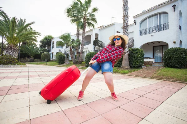 Reizen, vakantie en mensen concept - grappige vrouw trekt haar zware koffer en glimlachen — Stockfoto