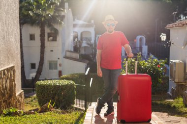 Seyahat, turizm ve insanlar kavramı - şapka ve gözlük otel arka plan üzerinde kırmızı çanta ile ayakta mutlu adam