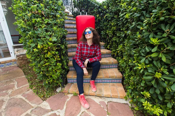 Holidays, travel, people concept - young woman in sunglasses sitting on stairs with suitcases and smiling — Stock Photo, Image