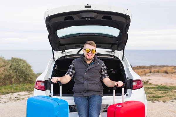 Cestování, turistiku a výlet koncept - mladý muž sedí v otevřeného kufru s dvěma kufry a usmívá se — Stock fotografie