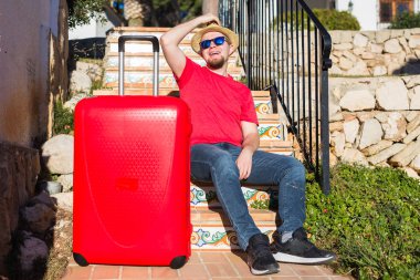 İnsanlar, tatil, seyahat ve dinlenme kavramı - bavulunu yakınındaki merdivenlerde oturan genç adam