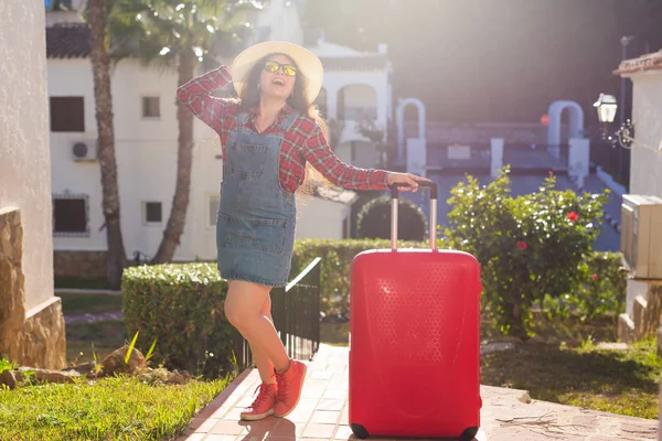 Viaje, vacaciones y concepto de verano - mujer joven con maleta de viaje roja llegó al hotel — Foto de Stock