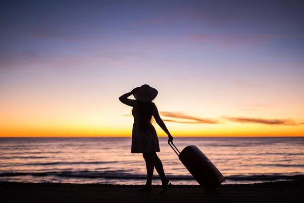 Relájese mujer con maleta en una playa al atardecer silueta. Concepto de viaje de vacaciones. Jovencita con maleta en el fondo del paisaje oceánico — Foto de Stock