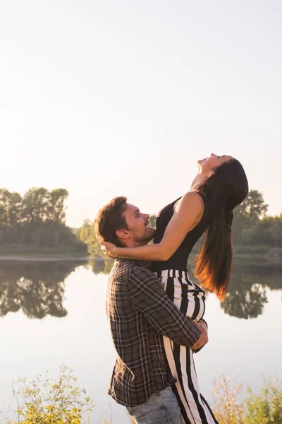 Romântico, pessoas e conceito de verão - homem levantou uma mulher em seus braços perto do lago ao pôr do sol — Fotografia de Stock