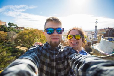 Komik genç çift kamera ile akıllı telefon Park Guell, Barselona, İspanya, gülümseyen fotoğrafı çekmek.