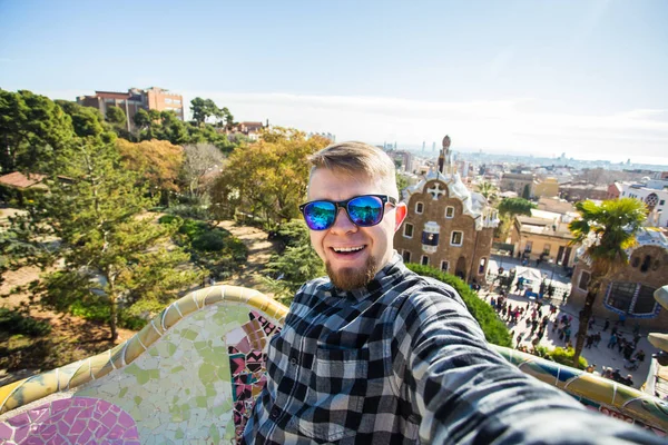 Подорожі та відпочинок концепції - красивий чоловік, дивлячись на фото беручи камери з смарт-телефону, посміхаючись в парк Гуель, Барселона, Іспанія. — стокове фото