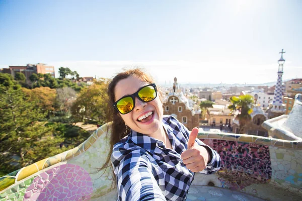 Подорожі та відпочинок концепції - красива молода жінка, дивлячись на фото беручи камери з смарт-телефону, посміхаючись в парк Гуель, Барселона, Іспанія. — стокове фото