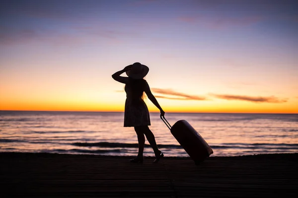 Relax woman with suitcase on a beach at sunset silhouette. Holiday travel concept. Young lady with suitcase on ocean landscape background