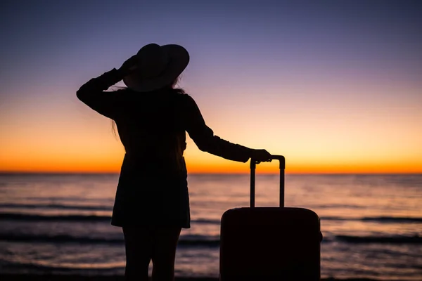 Relax donna con valigia su una spiaggia al tramonto silhouette. Concetto di viaggio vacanza. Giovane signora con valigia su sfondo paesaggio oceano — Foto Stock