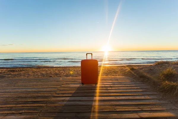Equipaje, vacaciones, concepto de viaje - una maleta roja de pie cerca del mar a la luz del sol — Foto de Stock