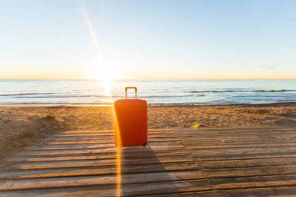 Equipaje, vacaciones, concepto de viaje - una maleta roja de pie cerca del mar a la luz del sol — Foto de Stock