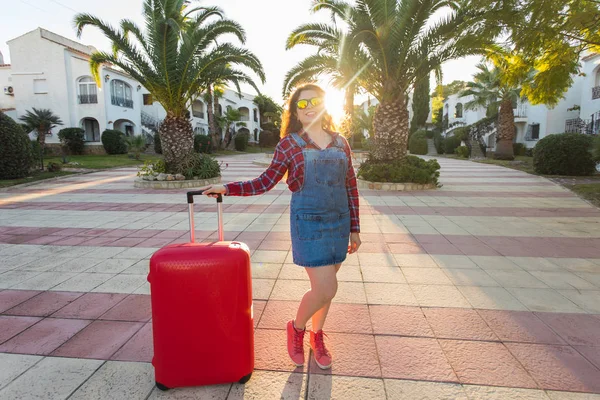 Viaje, vacaciones y concepto de verano - mujer joven con maleta de viaje roja llegó al hotel — Foto de Stock