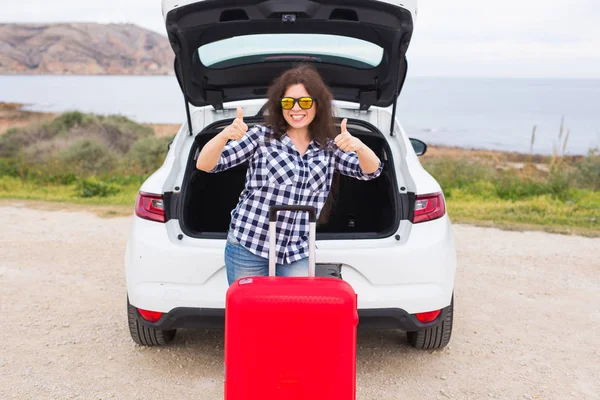 Lidé, dovolené a cestování koncept - mladá žena s kufrem ukazuje palec nahoru venku — Stock fotografie