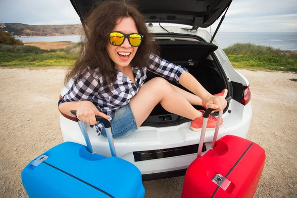 Dívka sedí v zadní části vozu s úsměvem a ukazuje palec. Smějící se dívka sedící v otevřeného kufru auta. Letní výlet — Stock fotografie