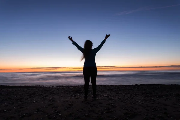 Vrijheid, vakantie en overwinning concept - silhouet van de vrouw met de handen omhoog terwijl je op het strand bij zonsondergang — Stockfoto