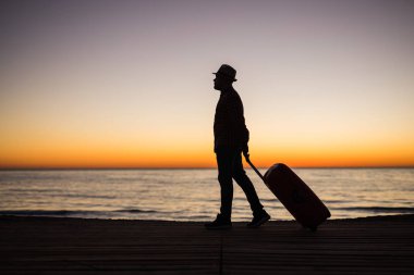 Gün batımı siluet bir kumsalda bavula adamla sakin ol. Tatil seyahat kavramı. Okyanus manzara arka plan bavula adamla