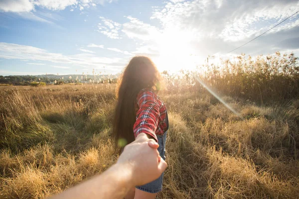 Traveling together. Follow me. Young woman holding boyfriends hand walking in the field on sunset