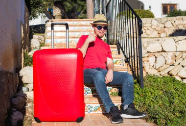 İnsanlar, tatil, seyahat ve dinlenme kavramı - bavulunu yakınındaki merdivenlerde oturan ve gösterilen genç adam yaşasın