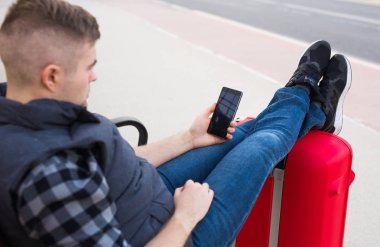 Seyahat, turizm ve insanlar kavramı - yakışıklı adam oturur ve ayakları bavula, içinde onun hareket eden bir şey koymak