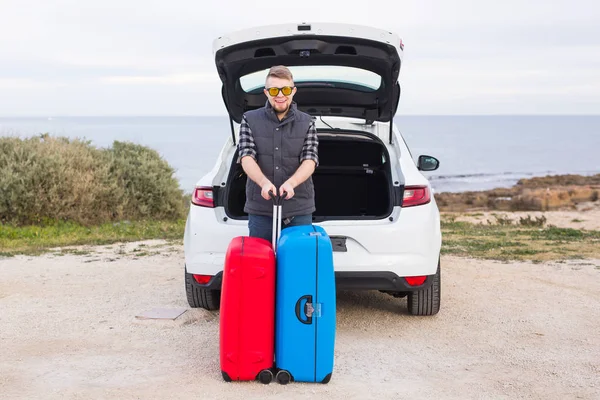 Cestování, cestovní ruch a lidé koncept - šťastný muž v brýlích, stojící nad pozadí přírody poblíž auto s kufry — Stock fotografie