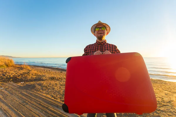 Concepto de viaje y verano - Turista masculino llevando una maleta roja en la playa — Foto de Stock