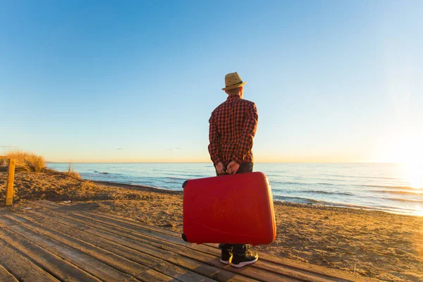 Viajes, vacaciones y concepto de verano - Vista trasera del hombre sosteniendo una maleta al atardecer — Foto de Stock