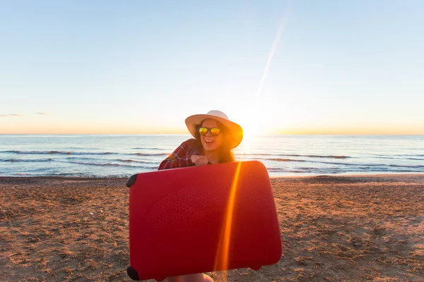Viajes, vacaciones y el concepto de la gente - Feliz mujer sonriente turista de pie cerca del mar con la maleta roja — Foto de Stock