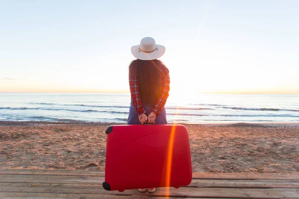 Vacanza, viaggio e turismo concetto - Indietro vista della donna con valigia rossa su sfondo spiaggia sabbiosa — Foto Stock