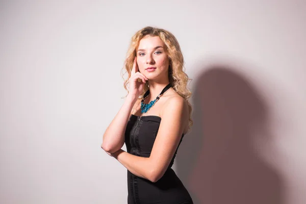 Conceito de moda e modelo - Linda jovem mulher loira sexy em um vestido preto posando contra uma parede branca com espaço de cópia — Fotografia de Stock