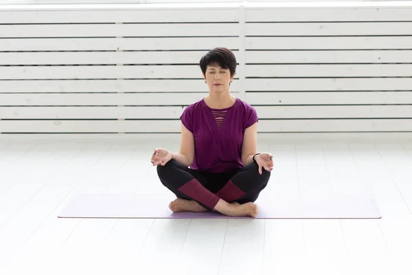 Yoga, harmony, people concept - Middle aged woman sitting in lotus position with closed eyes