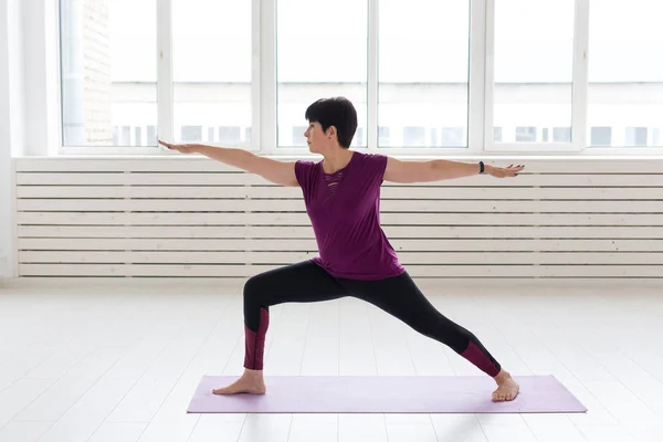 Gente, yoga, deporte y concepto de salud - Mujer de mediana edad de pie en Warrior sobre fondo blanco —  Fotos de Stock