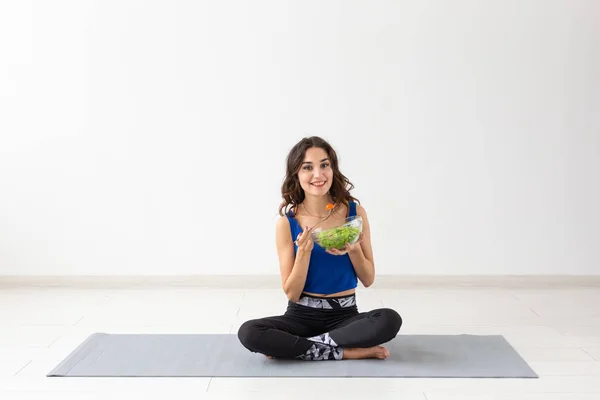 Estilo de vida saludable, personas y concepto deportivo - Mujer de yoga con un tazón de ensalada de verduras después de entrenar sobre fondo blanco — Foto de Stock