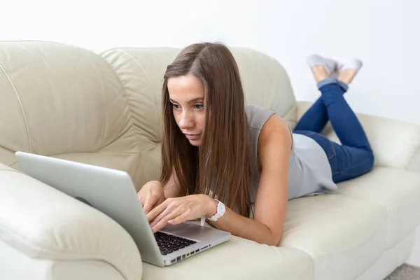 Koncepcja technologii, freelance i ludzie - młoda kobieta, leżąc na kanapie z laptopem — Zdjęcie stockowe
