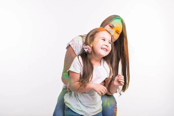 Family, festival of holi and holidays concept - Woman and little smiling girl covered with colourful powder over white background