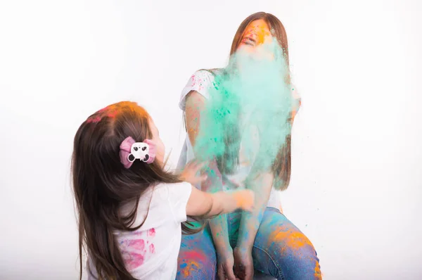 Фестиваль холи, веселья и людей концепции - мать и милая маленькая дочь играют с цветным порошком вместе на белом фоне — стоковое фото