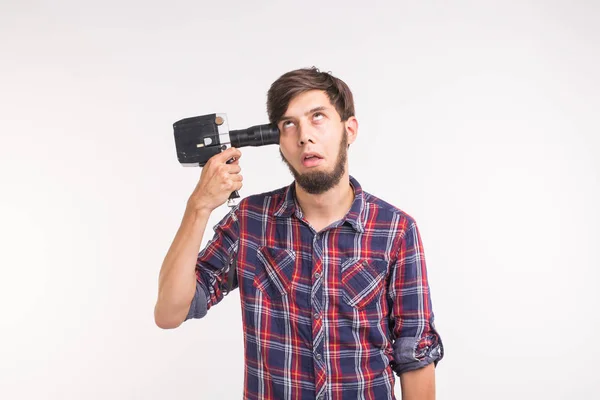 Broma, foto y concepto de gesto - joven divertido hombre tonto posando con la cámara cerca de su cabeza sobre fondo blanco — Foto de Stock