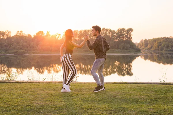 Romantic, social dance, people concept - young couple dancing near the lake in sunny day